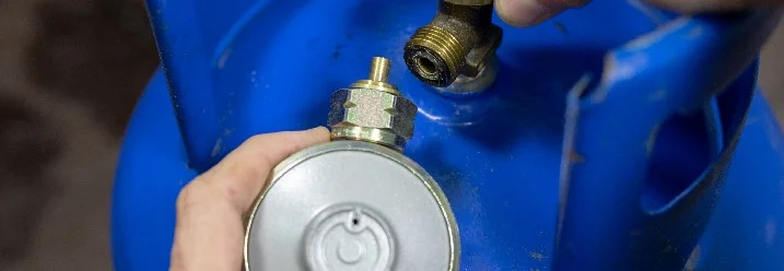 Person schließt Druckminderer an Gasflasche an